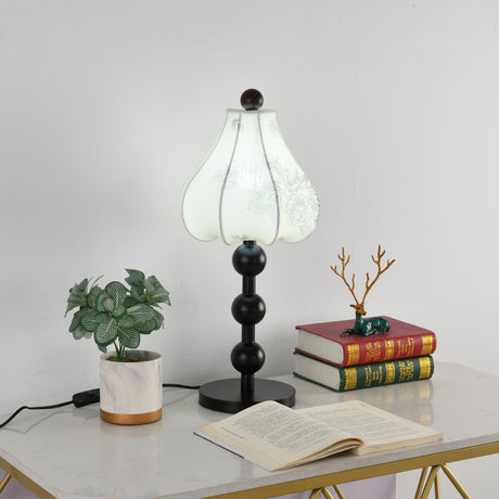 Floral table lamp unlit on a console beside stacked books and a plant