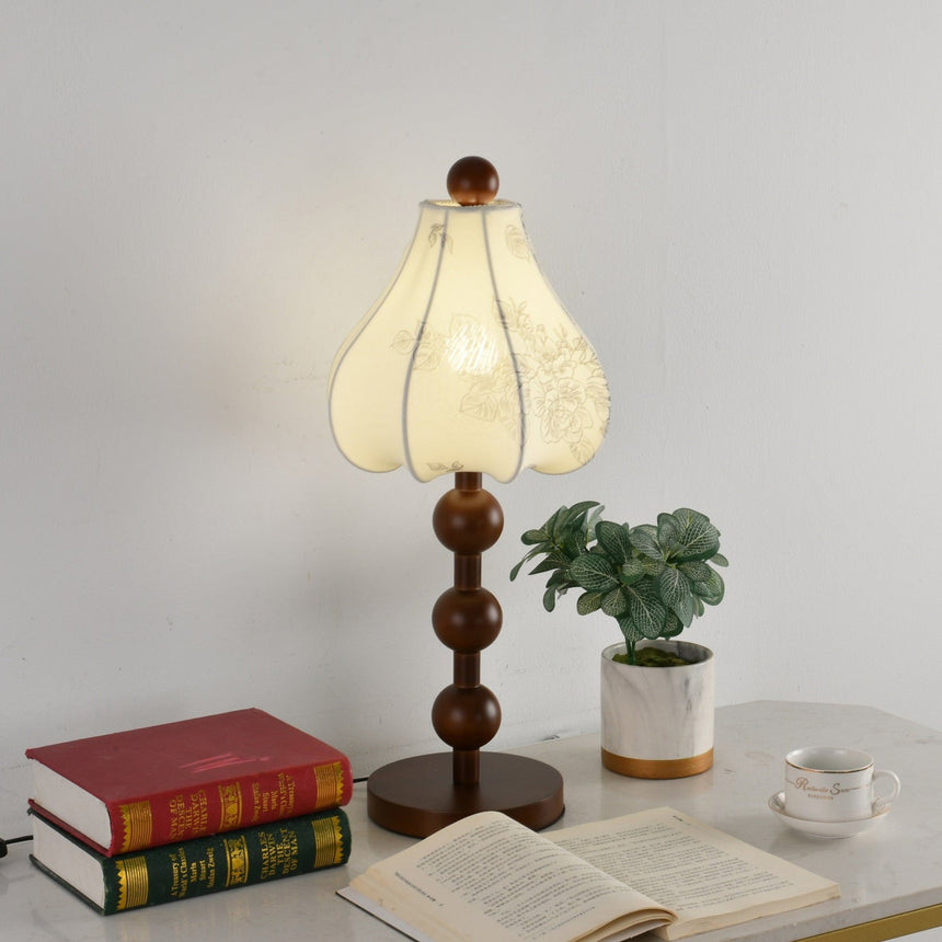 Walnut floral table lamp lit beside an open book and a small green plant