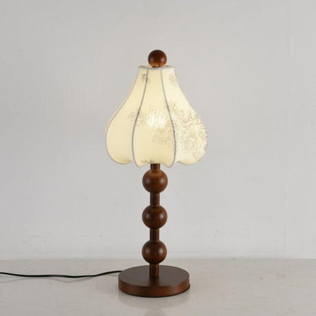 Walnut floral table lamp lit, the ribs of the petal shade showing through