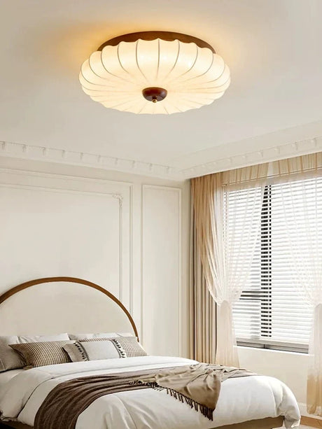 Pleated petal ceiling light above a bed beside a curtained window