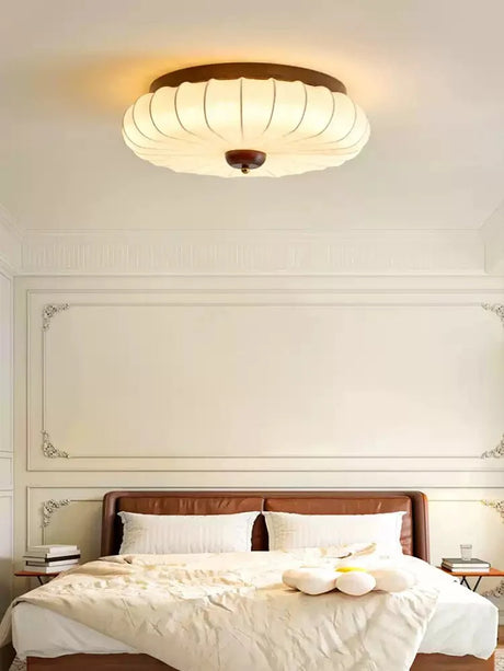 Pleated petal ceiling light above a bed with a wood headboard