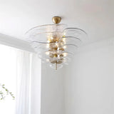 The clear glass petal shade lit under a white ceiling beside a pale curtain