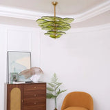 The green petal shade lit above a wooden cabinet with an orange armchair beside it