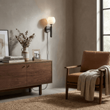 The lit lamp above a console with framed prints beside an armchair