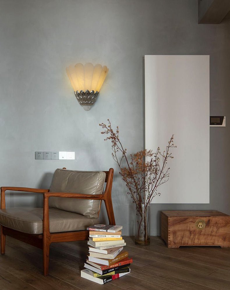 The sconce above a wood armchair with a stack of books and dried stems