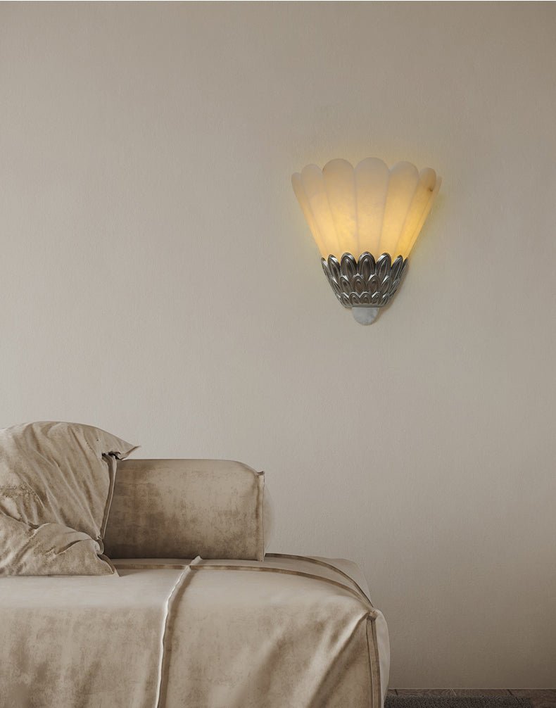 The sconce lit above a bed with a draped throw and soft pillows