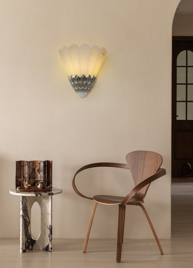 The sconce lit above a curved wood chair and a small side table