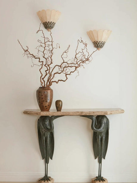 A pair of sconces above a sculptural console with a vase of branches