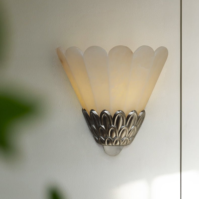 The sconce lit on a white wall beside a doorway and a leafy plant