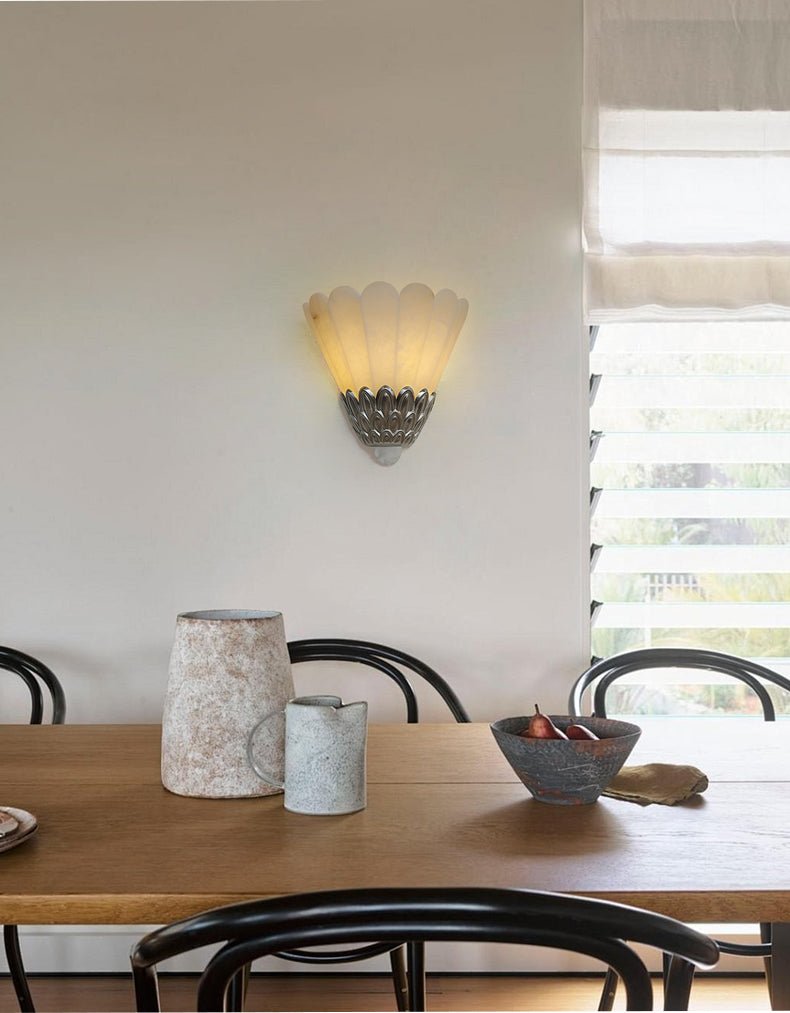 The sconce lit above a dining table with cane chairs and a candle