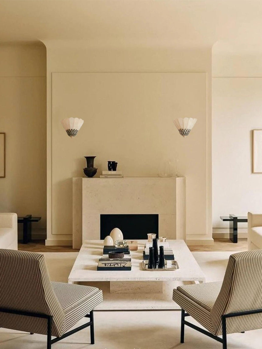 Two sconces on each side of a fireplace above armchairs and a low table