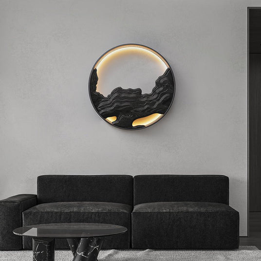 Carved disc lit on a pale wall above a dark sofa and a low table