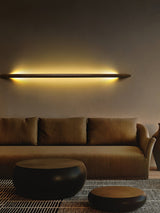 Rod lit horizontally on a warm wall above a low sofa and ottoman