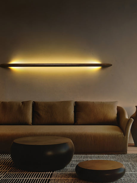 Rod lit horizontally on a warm wall above a low sofa and ottoman