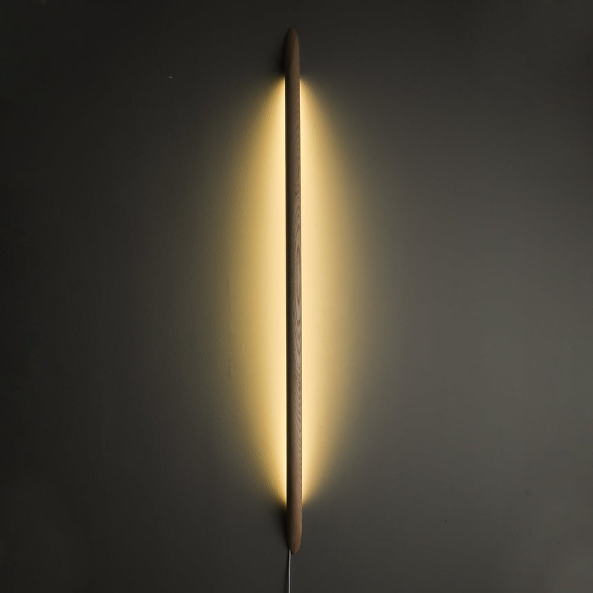 Dark rod lit vertically, the backglow washing the wall on both sides