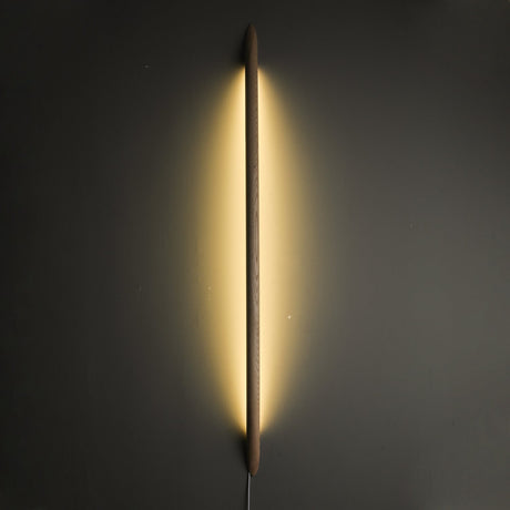 Long rod lit vertically on a dark wall, light spilling around it