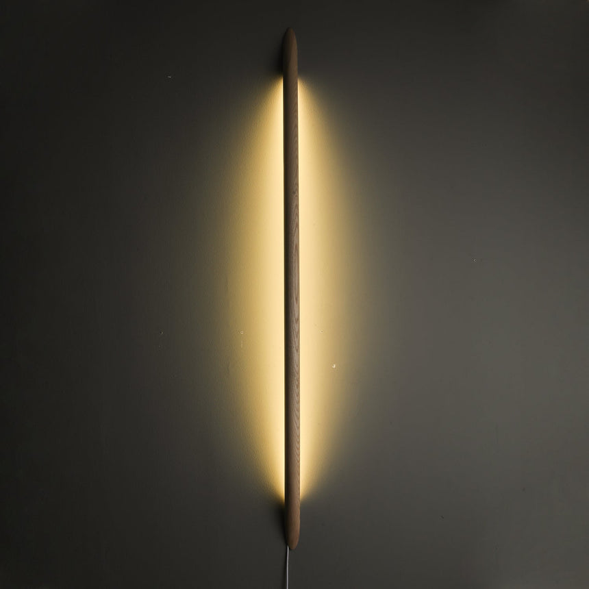 Long rod lit vertically on a dark wall, light spilling around it
