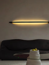 Rod lit horizontally above a dark curved sofa in a plain room