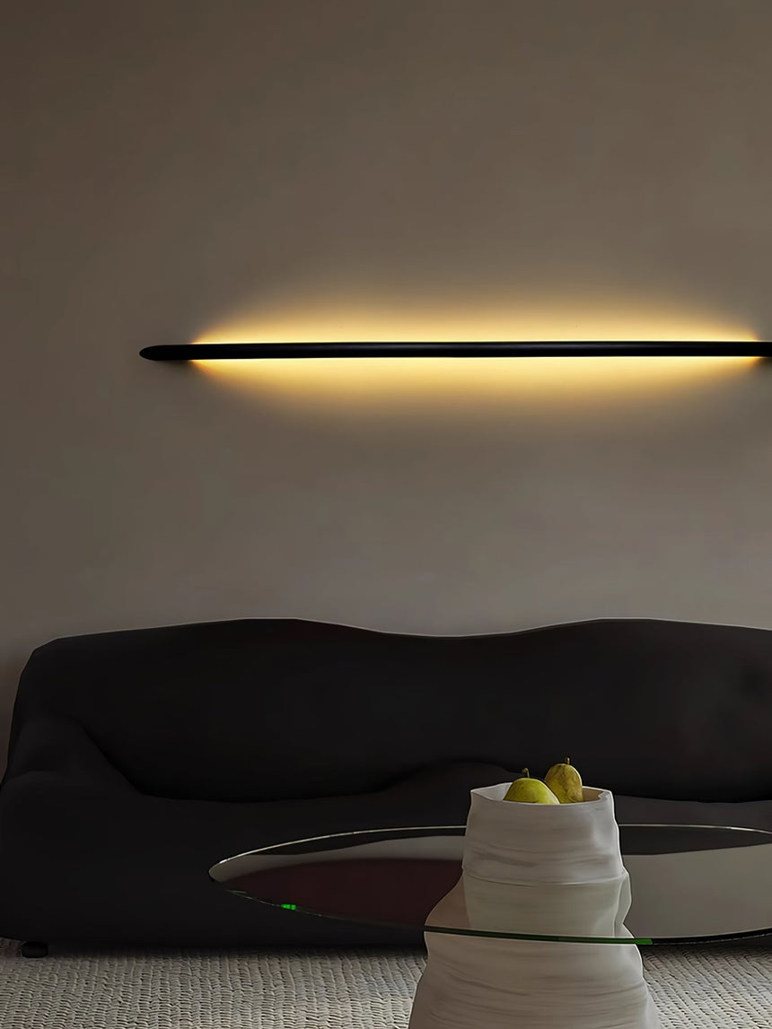 Rod lit horizontally above a dark curved sofa in a plain room