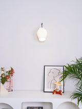 The small sconce above a white console with a framed drawing and a plant