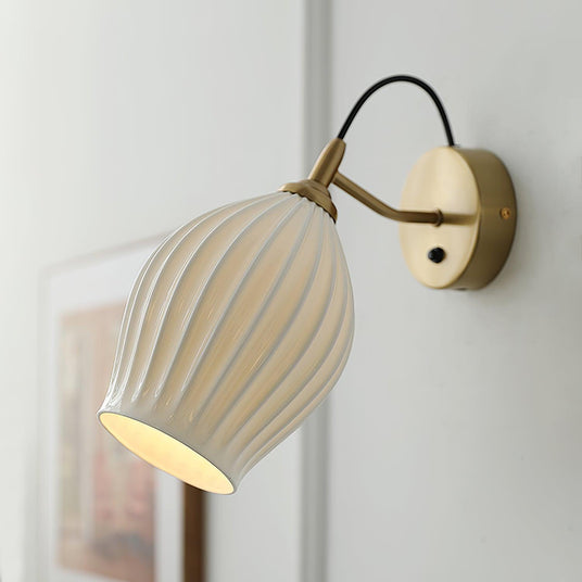 The fluted shade lit beside a framed print on a pale paneled wall