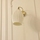 The fluted shade lit on a cream paneled wall with molding