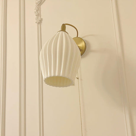 The fluted shade lit on a cream paneled wall with molding