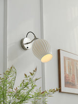 The sconce lit on a pale wall beside a framed picture and a leafy plant