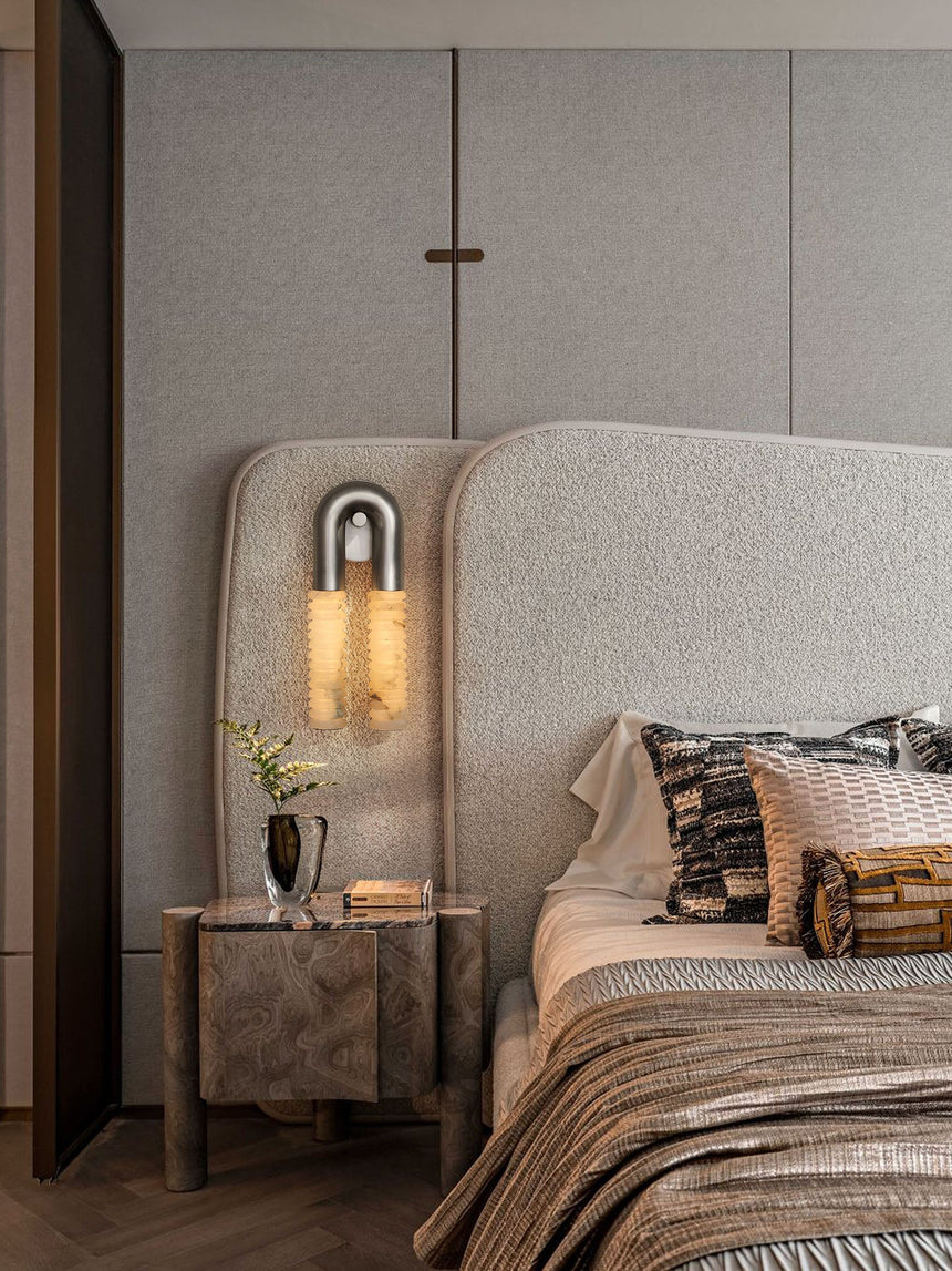 The sconce lit in a bedroom above a nightstand with books and a bed