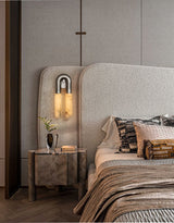 The sconce lit above a nightstand beside a bed with a woven headboard