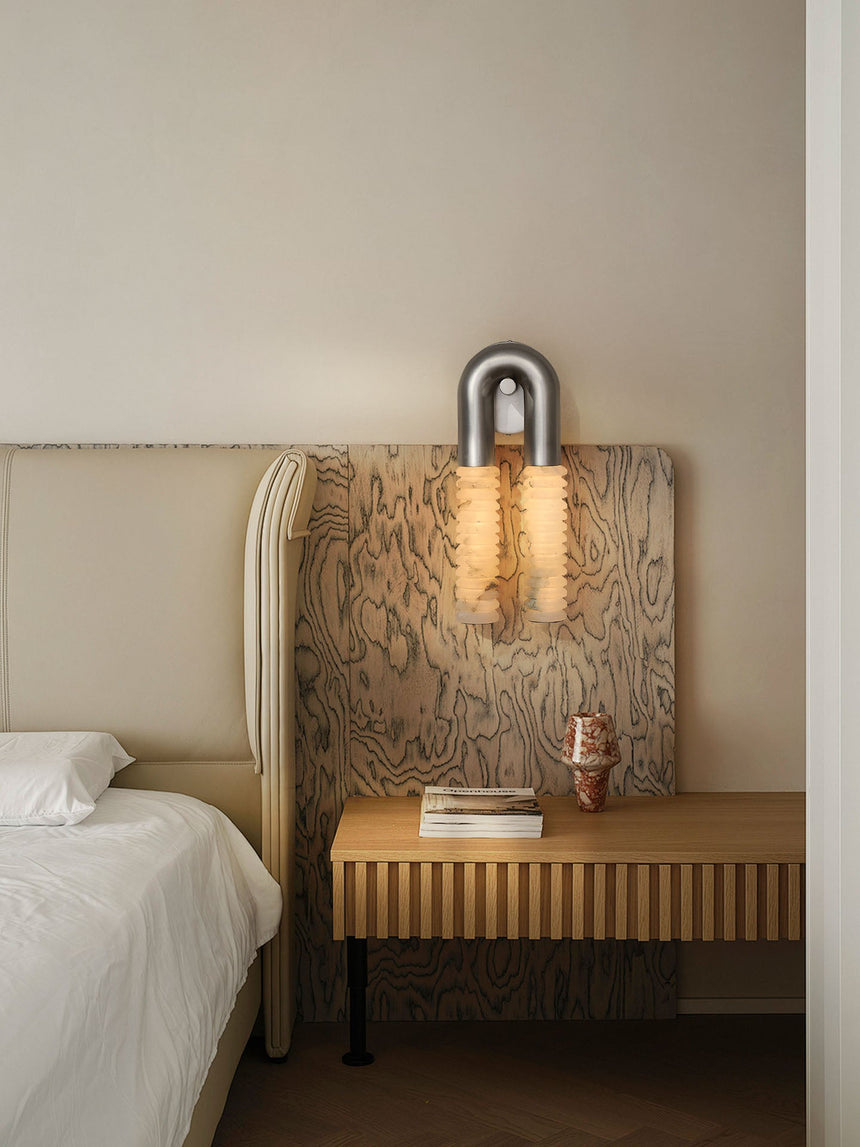 The sconce lit above a wood bench beside a bed with white linens