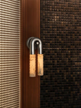 The lit sconce against a woven panel, the ribbed stone catching the light