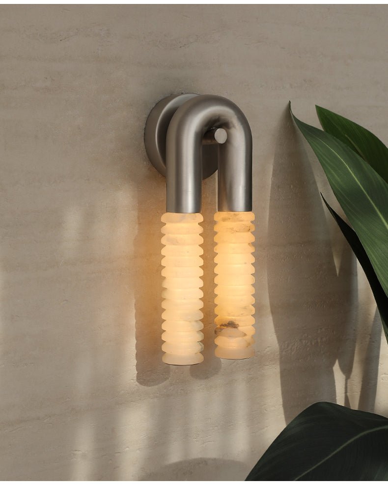 The lit sconce on a plaster wall beside a broad green leaf