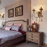 Two sconces on a bedroom wall beside framed prints above a bed and a chest