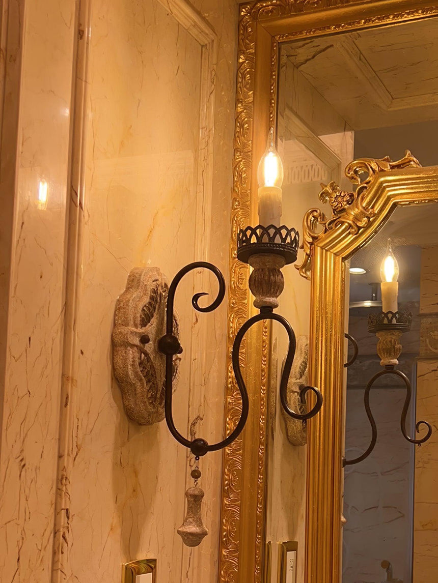 Sconce lit beside a gilt mirror, the candle lamps reflected in the glass