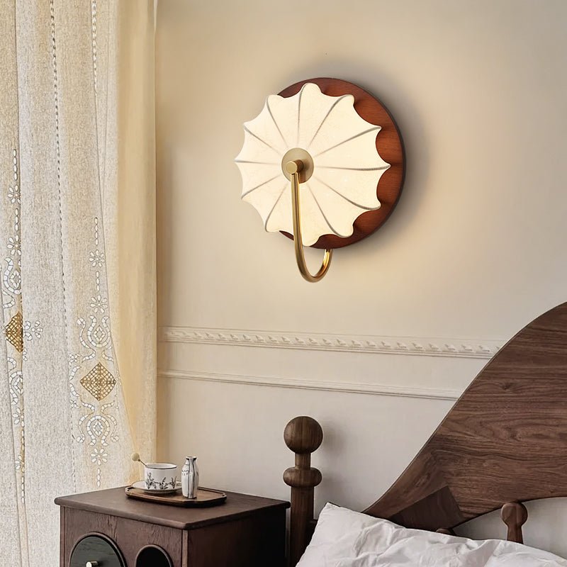Sconce lit beside a bed with a wood headboard, a nightstand and a curtain
