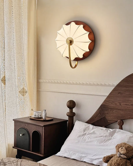 Sconce lit beside a bed above a nightstand with a small teddy on it