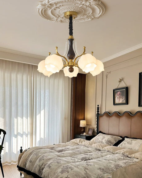 Glass chandelier lit in a bedroom above a bed with a padded headboard