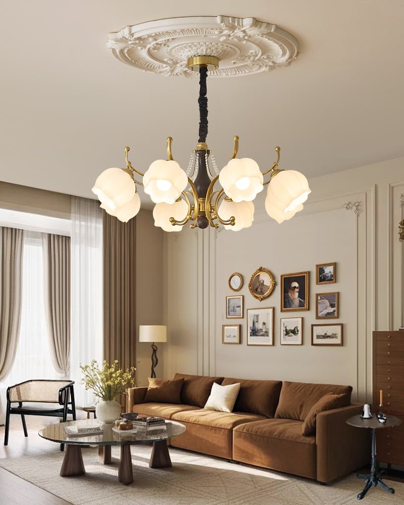 Chandelier lit in a living room above a brown sofa and framed art