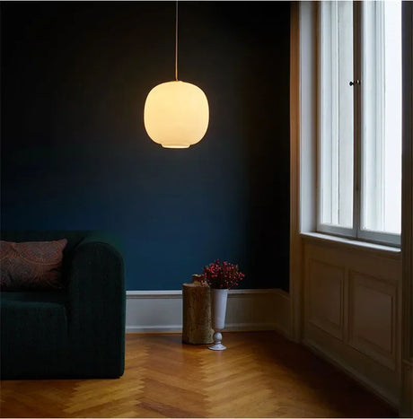 A frosted globe lit in a dark room beside a window and a green chair