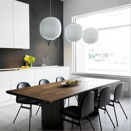 Three frosted globes lit above a long wooden table in a bright kitchen