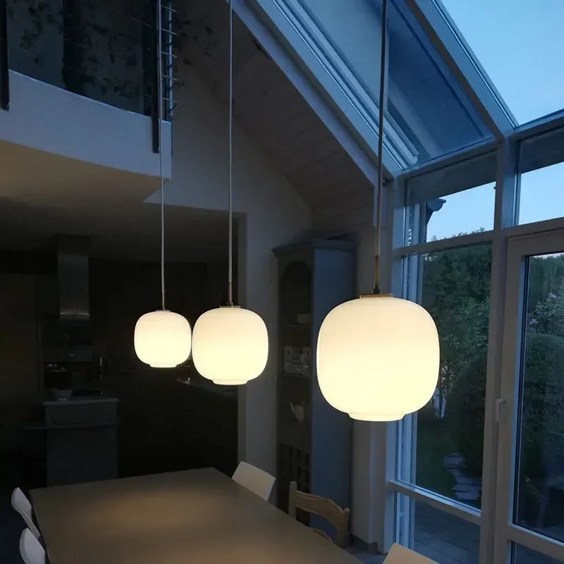 Three frosted globes lit in a row beside tall windows at dusk