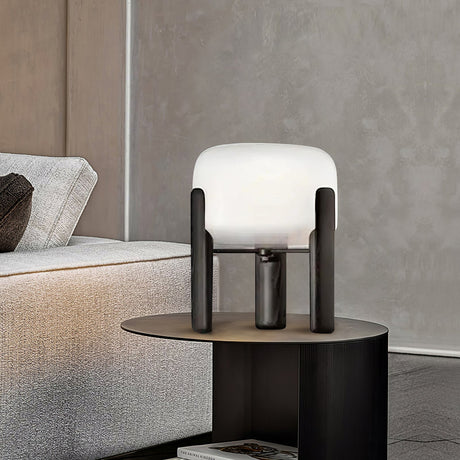 Frosted glass table lamp lit on a dark side table beside a sofa