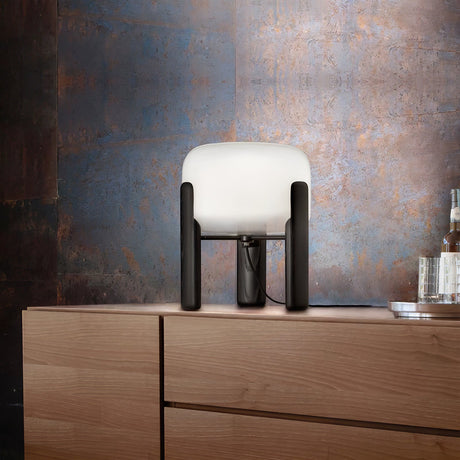 Frosted glass table lamp lit on a wood dresser against a patina wall