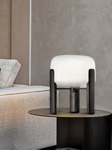 Frosted glass table lamp lit on a round side table beside a bed