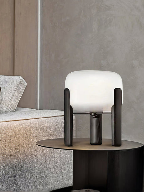 Frosted glass table lamp lit on a round side table beside a bed