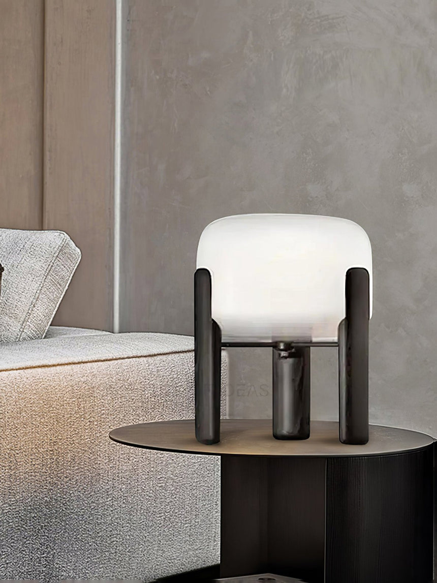 Frosted glass table lamp lit on a round side table beside a bed