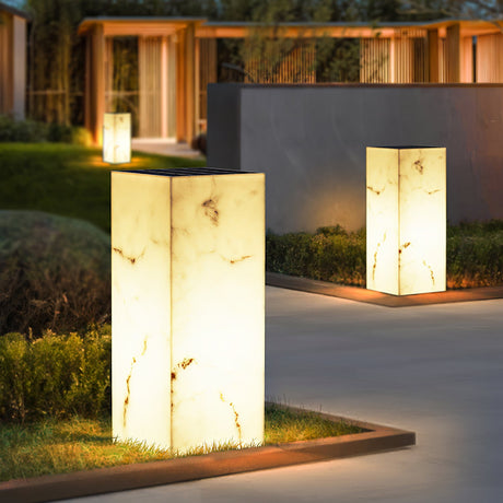 Two lit at the edge of a grass strip beside pale terrace paving