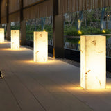Four lit in a line along a paved walk beside a lit timber screen
