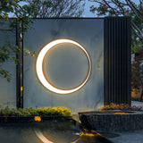 The ring lit on a stone wall above a still pool and a planted edge at dusk
